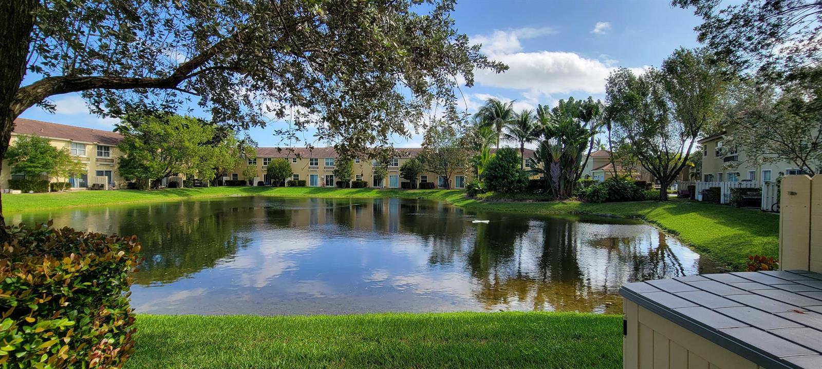 A view of a pond surrounded by apartment buildings and green lawns under a blue sky — 2851 W Prospect Road # 1102, Tamarac FL 33309, TAMARAC, FL