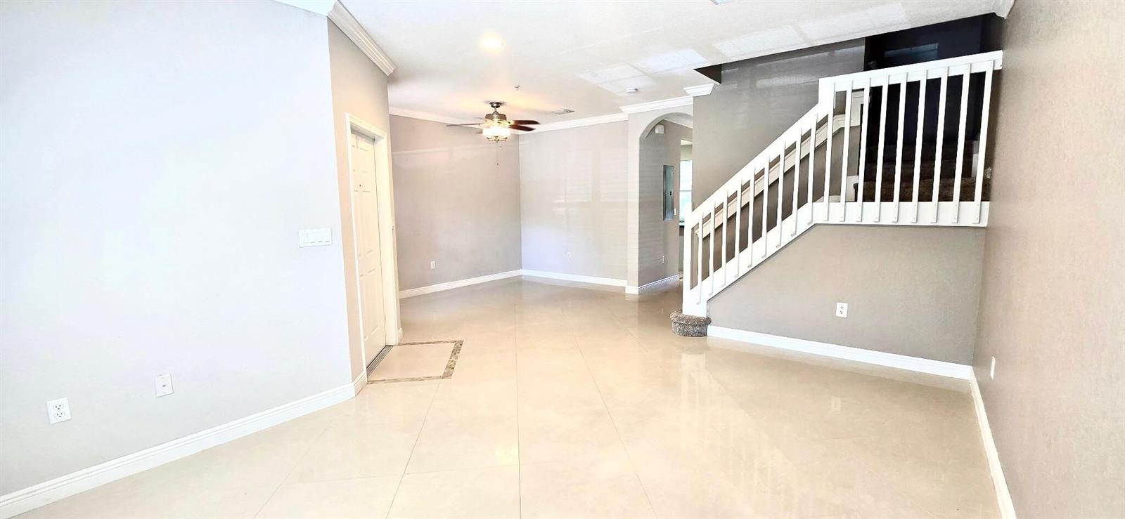 An open-concept living area features light-colored tile flooring, a white staircase, and a ceiling fan — 2851 W Prospect Road # 1102, Tamarac FL 33309, TAMARAC, FL