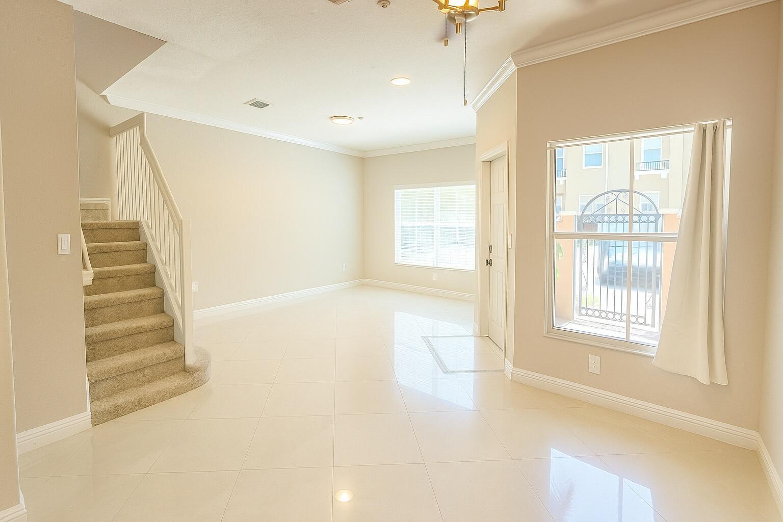 An empty room with beige walls, light tile flooring, a carpeted staircase, and large windows — 2851 W Prospect Road # 1102, Tamarac FL 33309, TAMARAC, FL