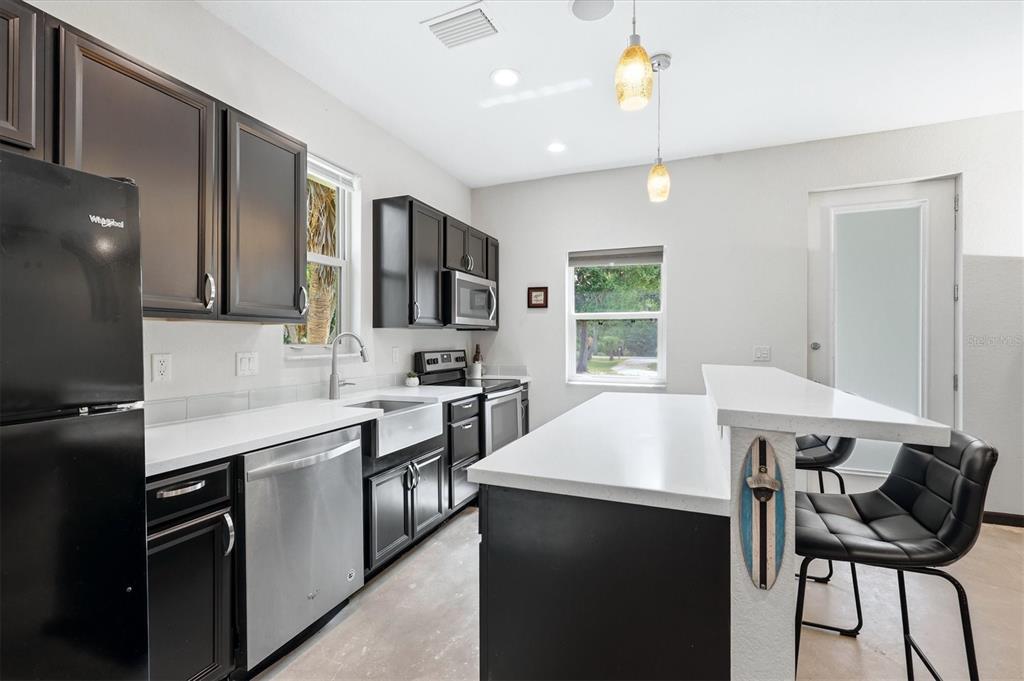 A kitchen features dark cabinets, white countertops, stainless steel appliances, and a breakfast bar — 788 HARMONY LANE, ENGLEWOOD, FL