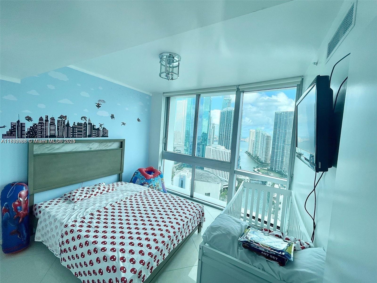 A bedroom features a Spider-Man themed bed, a crib, and floor-to-ceiling windows overlooking a city — 350 S Miami Ave # 3602, Miami FL 33130, MIAMI, FL