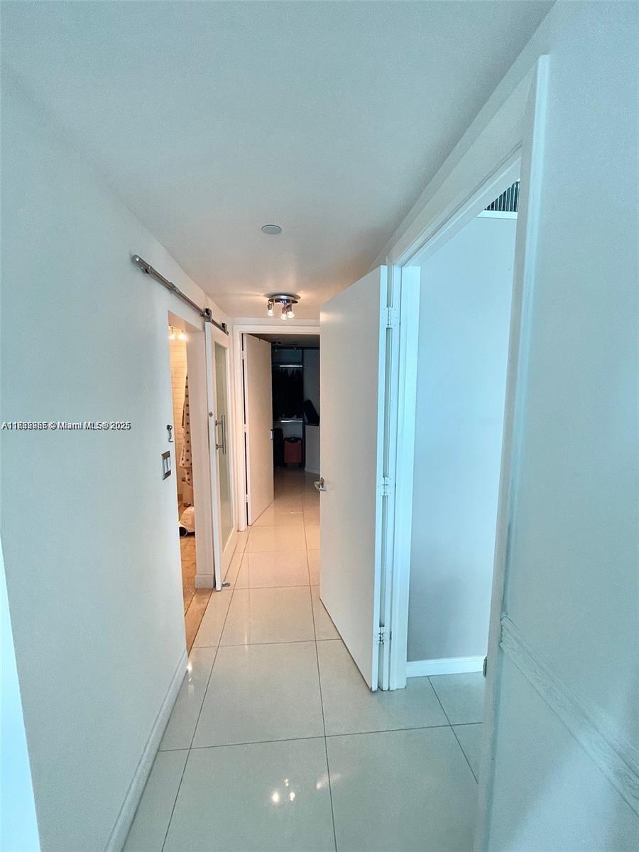 A hallway with white walls, tiled floors, and multiple doorways leads toward a distant room — 350 S Miami Ave # 3602, Miami FL 33130, MIAMI, FL