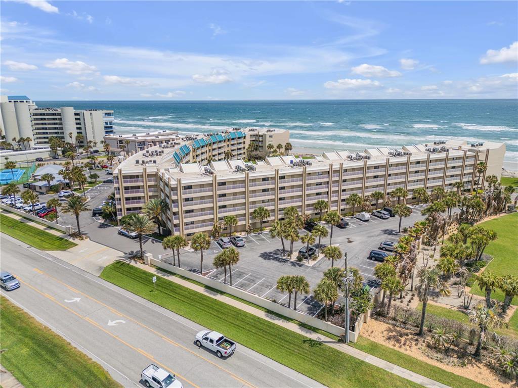 An aerial view of a multi-story beachfront condominium complex with a parking lot and palms — 4501 S ATLANTIC AVENUE UNIT 1150, NEW SMYRNA BEACH, FL