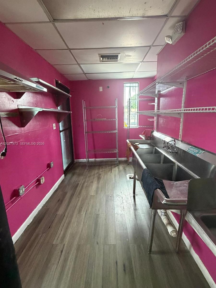 A commercial kitchen features pink walls, wood-look flooring, a three-compartment sink, and metal shelving — 139 NE 1st Ave, Hallandale Beach FL 33009, HALLANDALE BEACH, FL