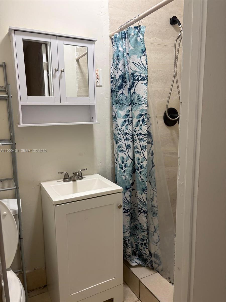 A small bathroom features a white vanity, a wall-mounted cabinet, and a floral shower curtain — 1384 NW 27th St # 1382, Miami FL 33142, MIAMI, FL
