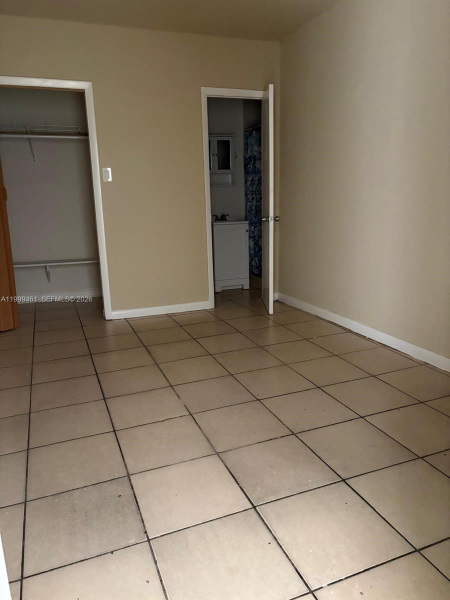 A room with beige tile flooring, a walk-in closet, and an open bathroom door — 1384 NW 27th St # 1382, Miami FL 33142, MIAMI, FL