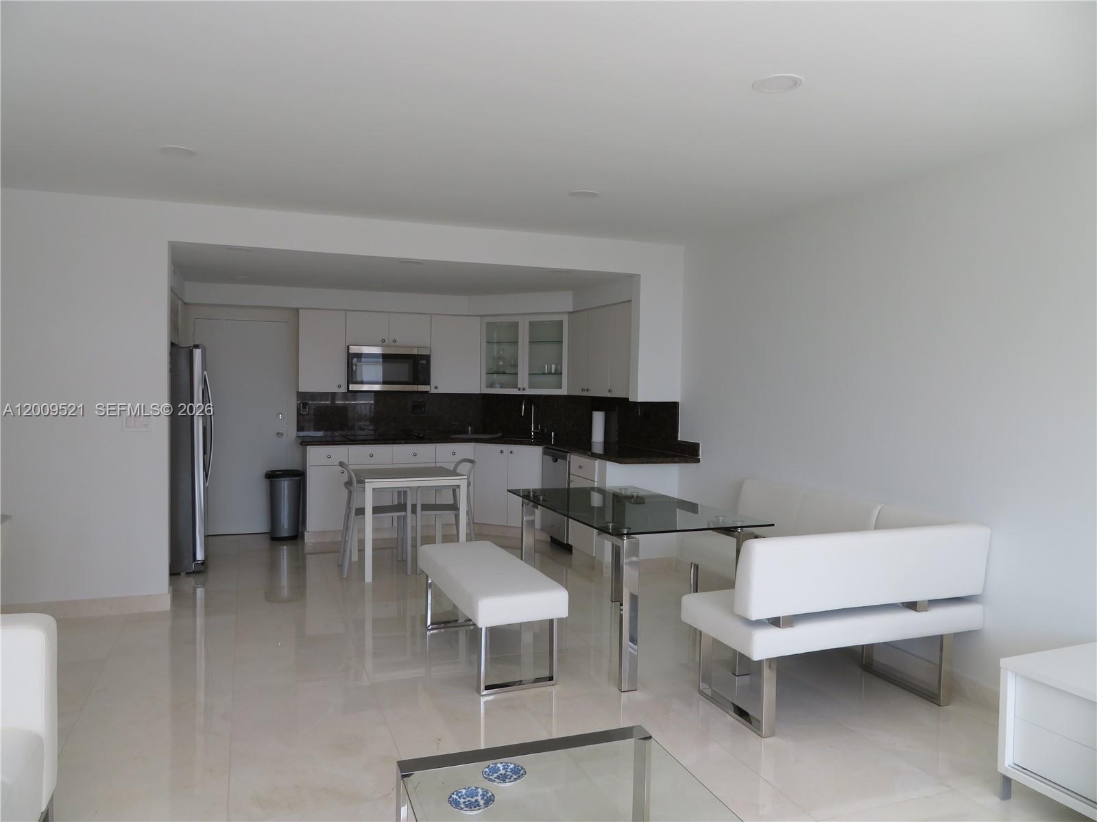 A modern kitchen with white cabinets and a dining area featuring a glass table — 1408 Brickell Bay Dr # 1002, Miami FL 33131, MIAMI, FL