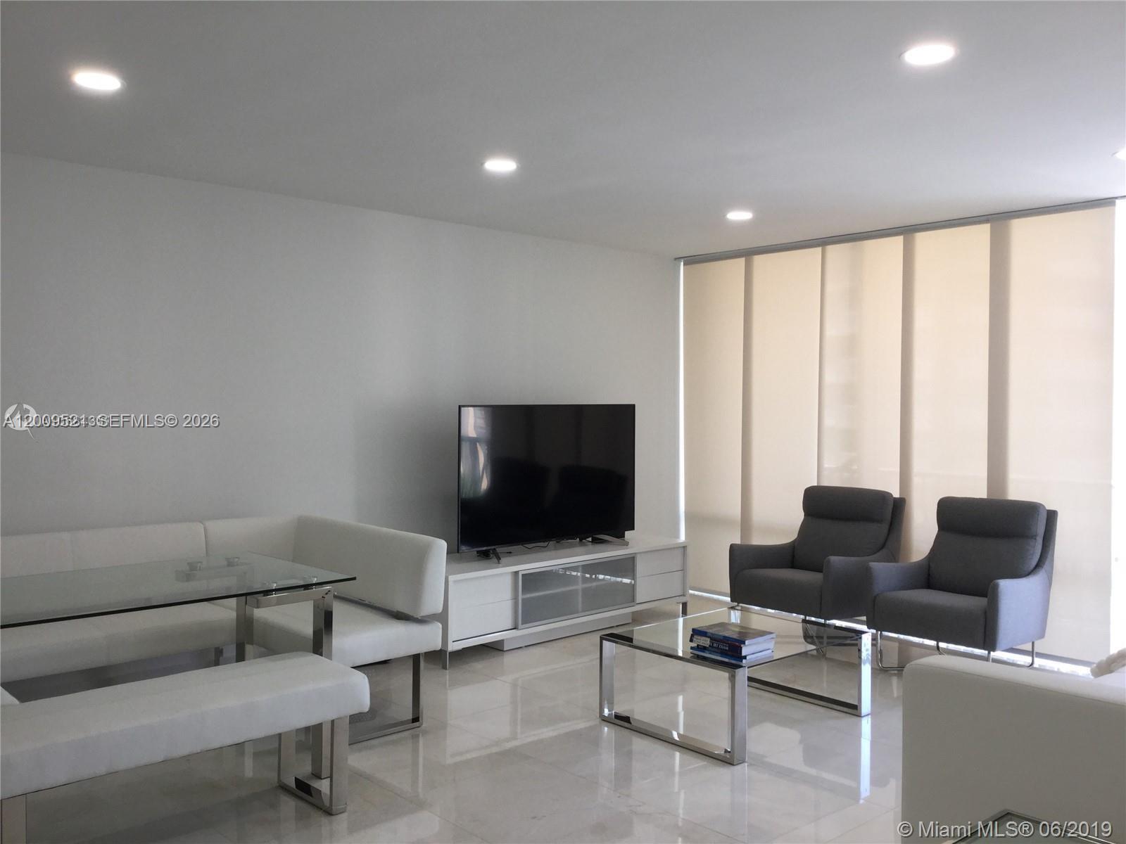 A modern living room features white furniture, a glass coffee table, and two grey armchairs — 1408 Brickell Bay Dr # 1002, Miami FL 33131, MIAMI, FL
