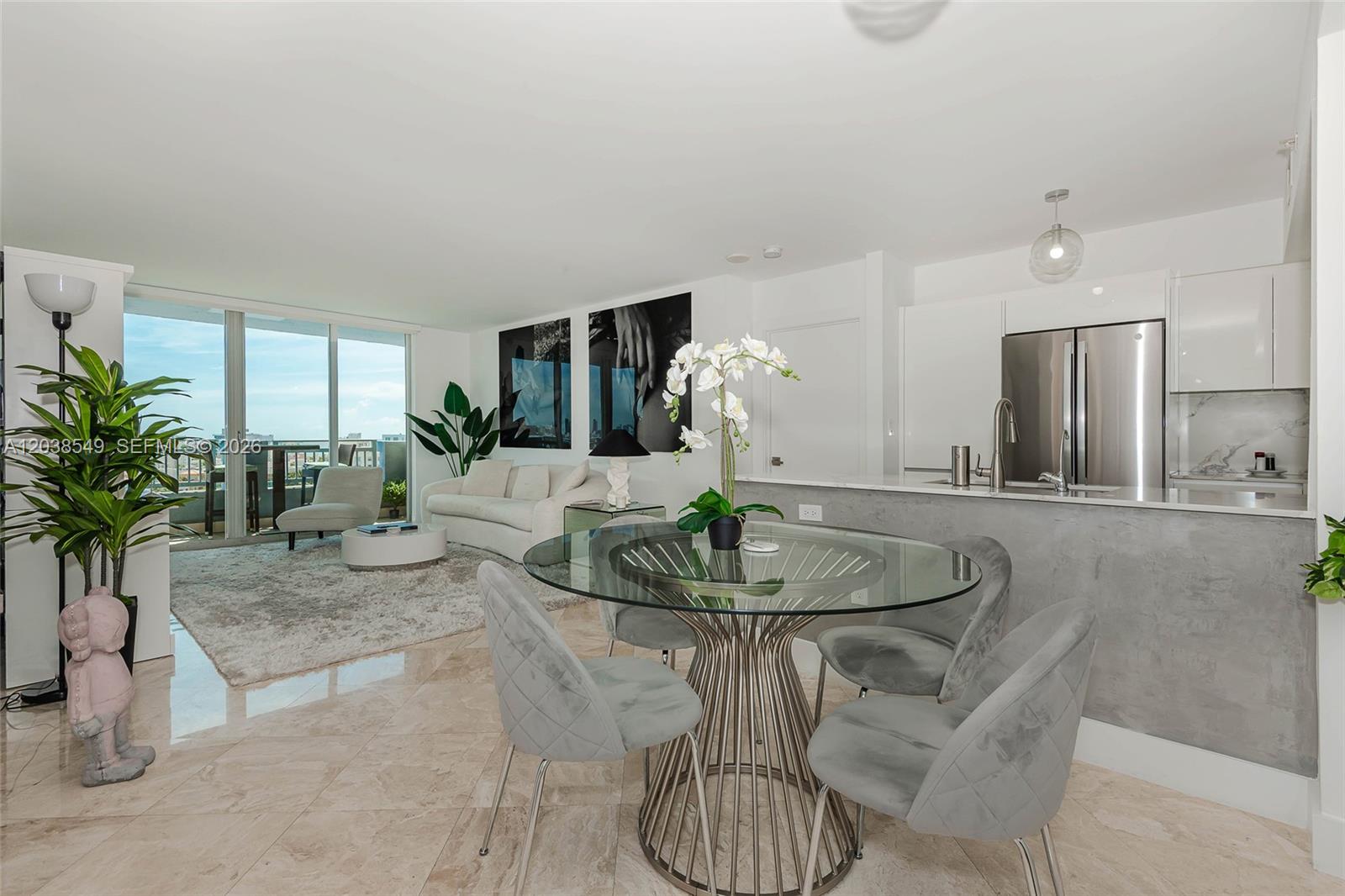 A modern open-concept living and dining area features a glass table, gray chairs, and balcony — 90 Alton Rd # 1109, Miami Beach FL 33139, MIAMI BEACH, FL