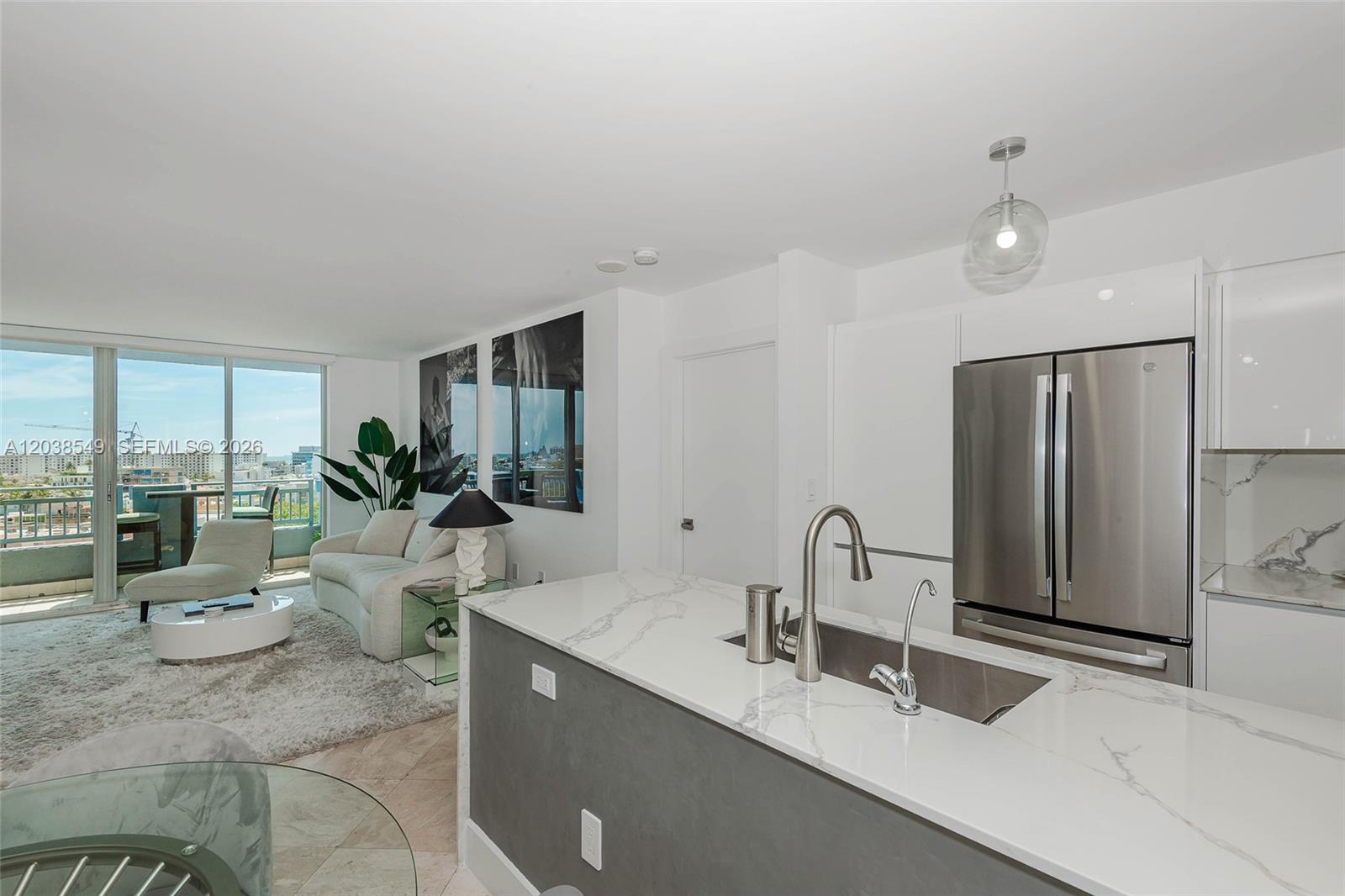 A modern kitchen with a marble-topped island overlooks a living area with a balcony view — 90 Alton Rd # 1109, Miami Beach FL 33139, MIAMI BEACH, FL