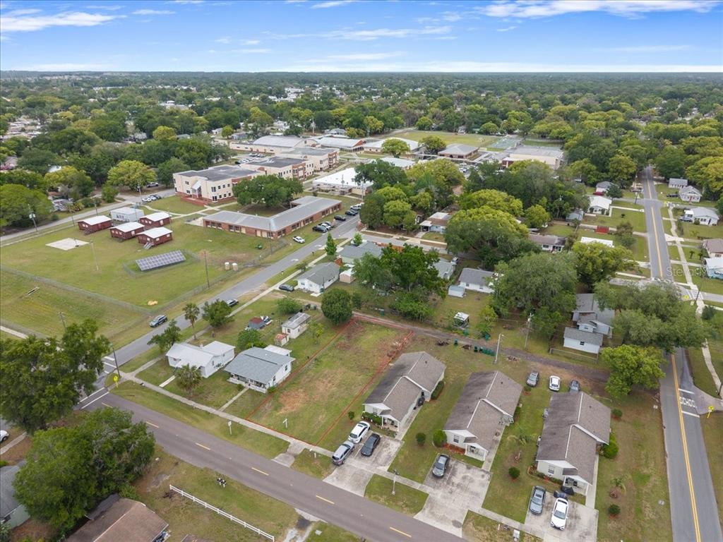 An aerial view shows a vacant residential lot situated between several houses and a school — 5540 8TH STREET, ZEPHYRHILLS, FL