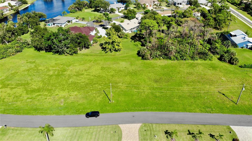 An aerial view shows a vacant, grassy residential lot bordered by a road and trees — 17504 CUILLAGAN COURT, PUNTA GORDA, FL