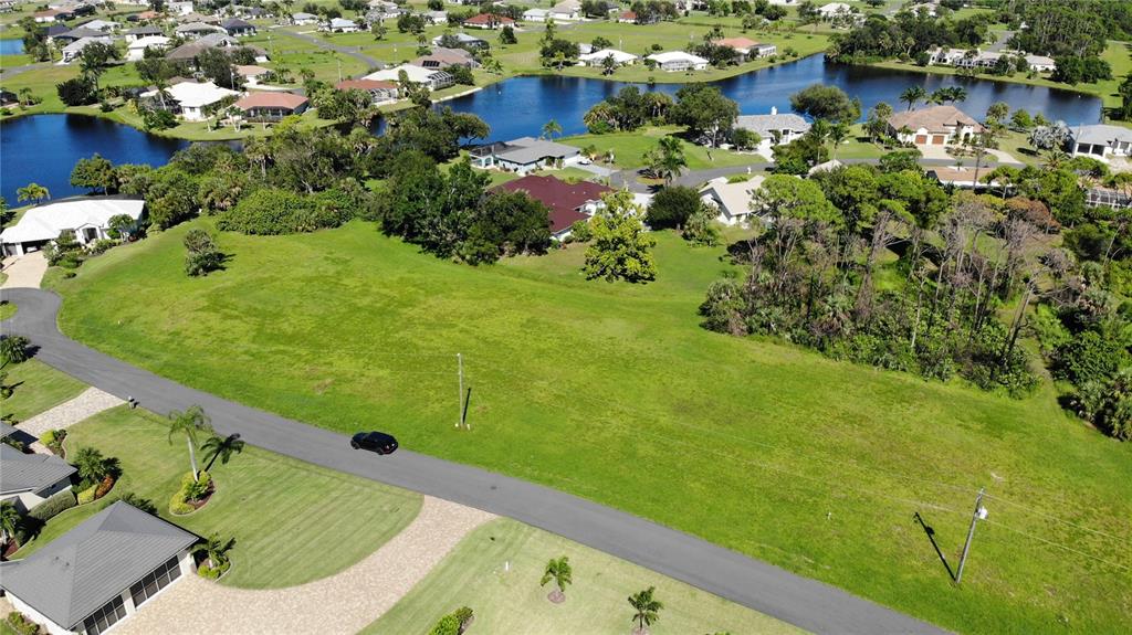 An aerial view shows a vacant grassy lot situated along a curved residential street — 17504 CUILLAGAN COURT, PUNTA GORDA, FL
