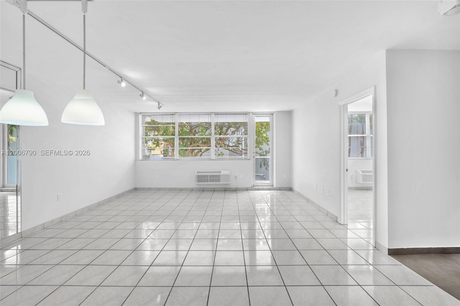 An empty, white-walled living room features light-colored tile flooring and two hanging pendant lights — 5313 Collins Ave # 204, Miami Beach FL 33140, MIAMI BEACH, FL
