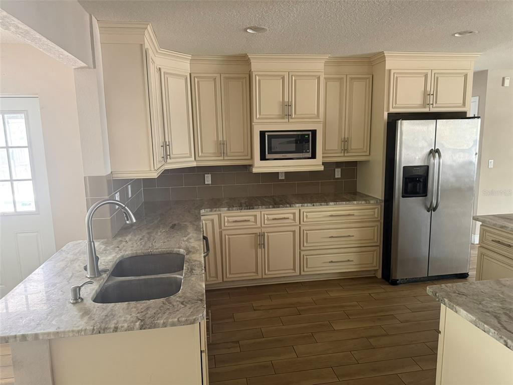 A kitchen features cream-colored cabinets, granite countertops, stainless steel appliances, and wood-look tile flooring — 4207 21 ST AVENUE W, BRADENTON, FL