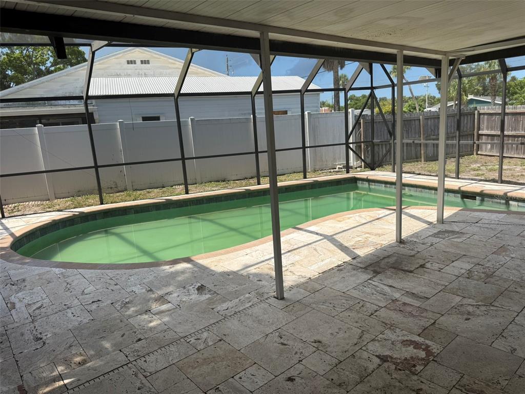 A screened-in patio with stone pavers overlooks a green swimming pool and fenced yard — 4207 21 ST AVENUE W, BRADENTON, FL