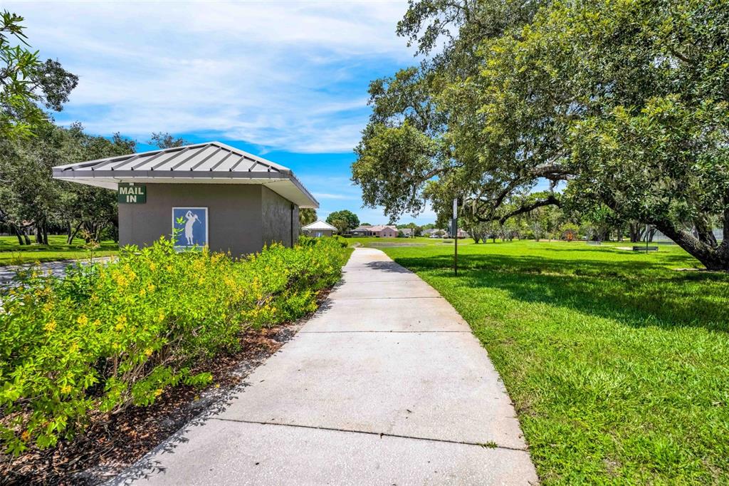 A concrete path leads past a small building with a mail station and golf signage — 9322 SEVE COURT, WEEKI WACHEE, FL