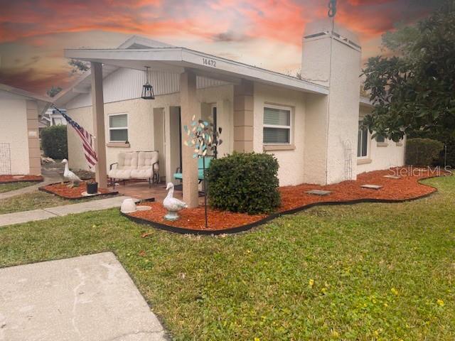 A single-story house with a covered porch, stucco exterior, and red mulch landscaping — 14472 VALENTINE DRIVE, LARGO, FL