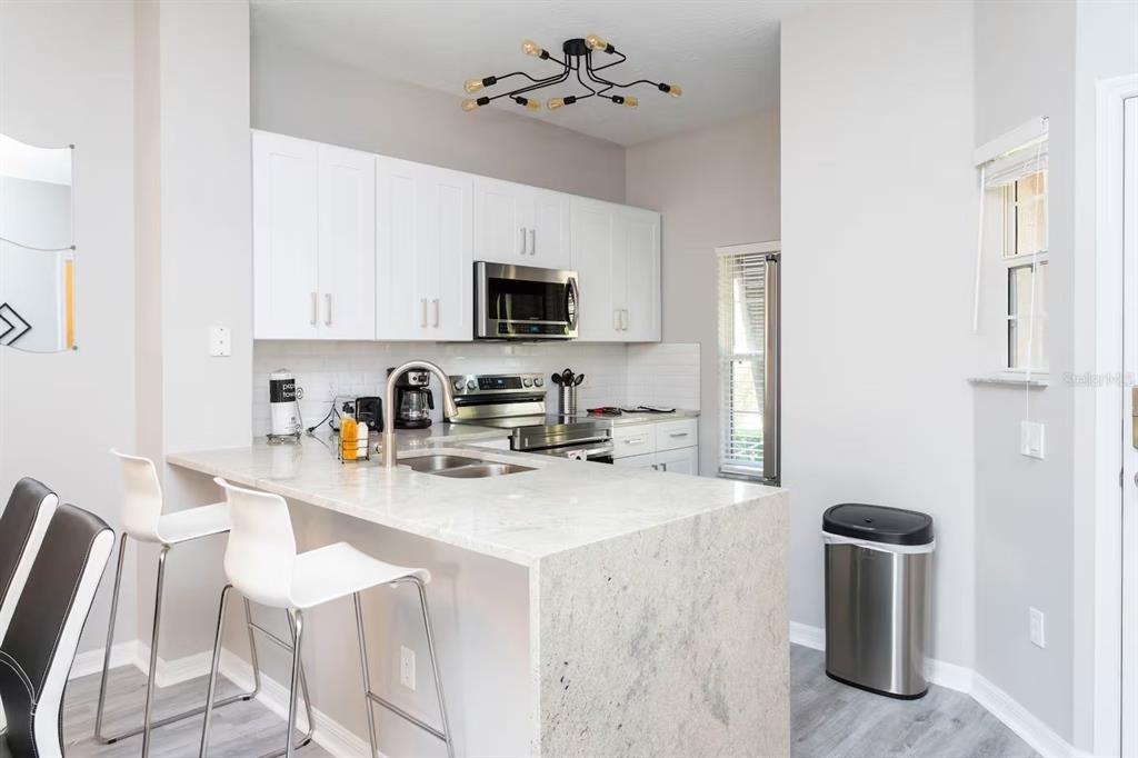 A modern kitchen features white cabinets, granite countertops, a breakfast bar, and stainless steel appliances — 4505 ALBERTO CIRCLE, KISSIMMEE, FL