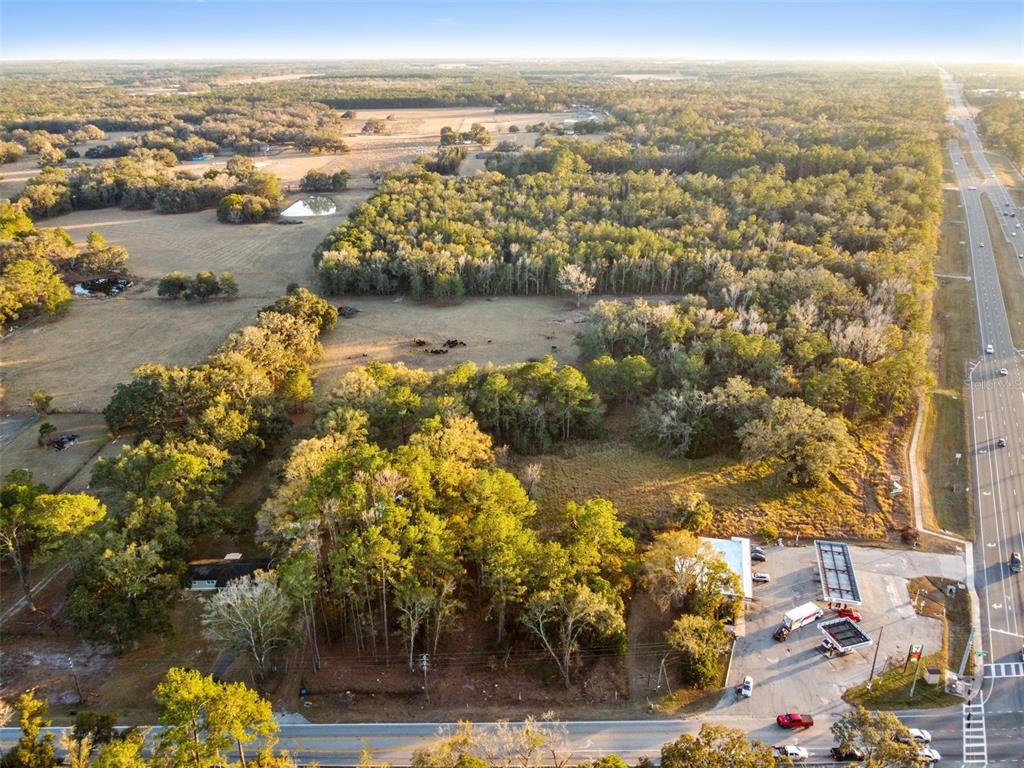 An aerial view shows a wooded lot, open pasture, and a gas station near a highway — POWELL ROAD, BROOKSVILLE, FL
