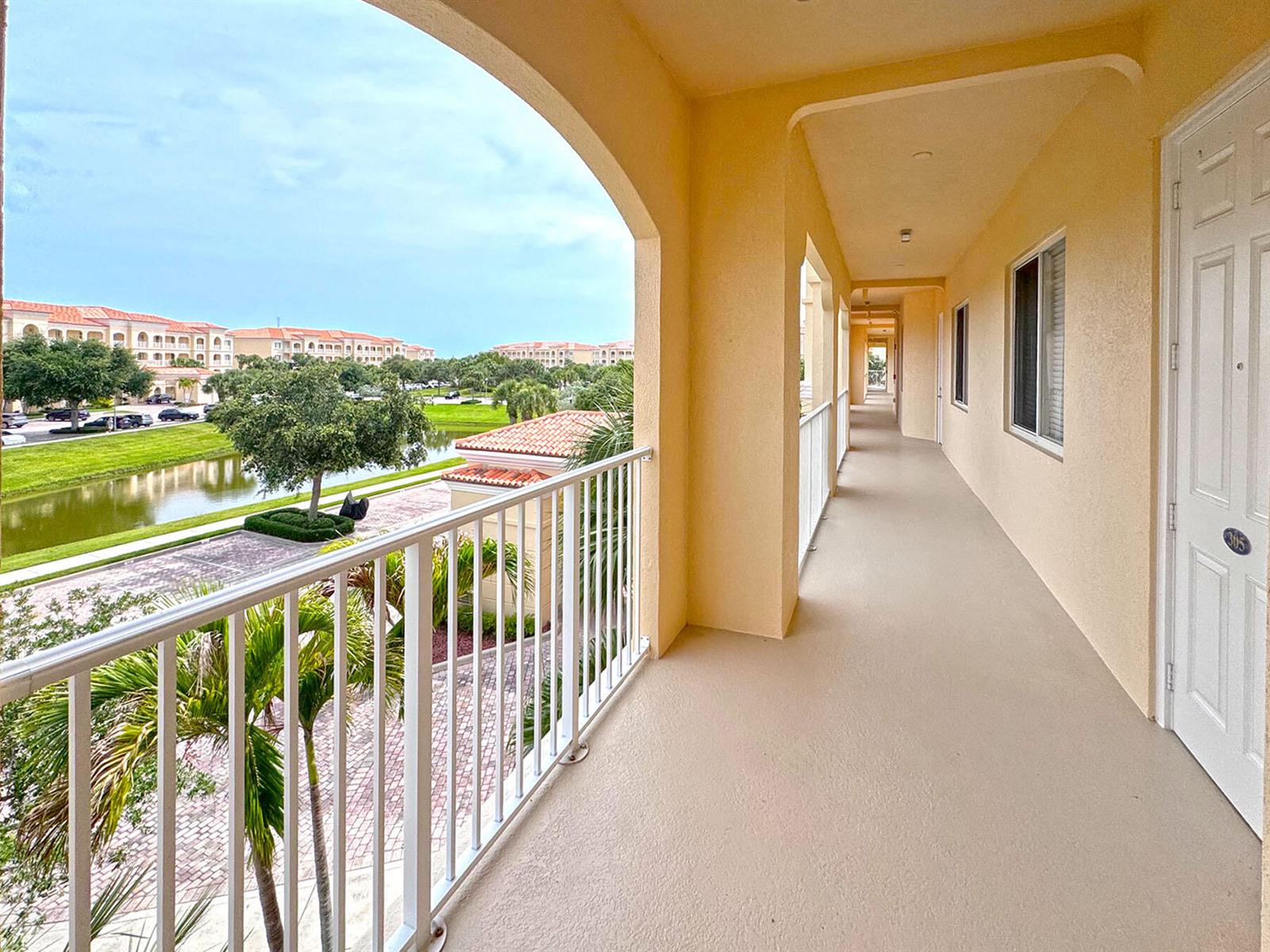 An outdoor covered walkway with a white railing overlooks a pond and residential buildings — FORT PIERCE, FL