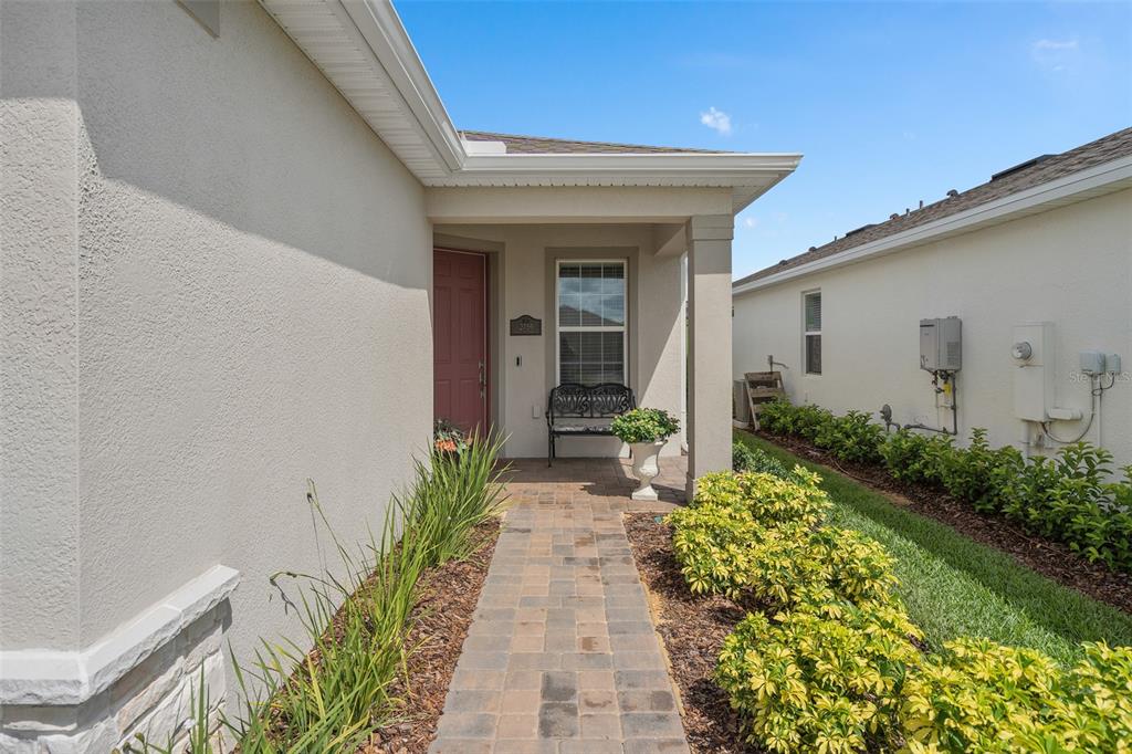 A paved walkway leads to the covered entryway of a house with a red door — 2759 PURPLE MEADOW COURT, MINNEOLA, FL