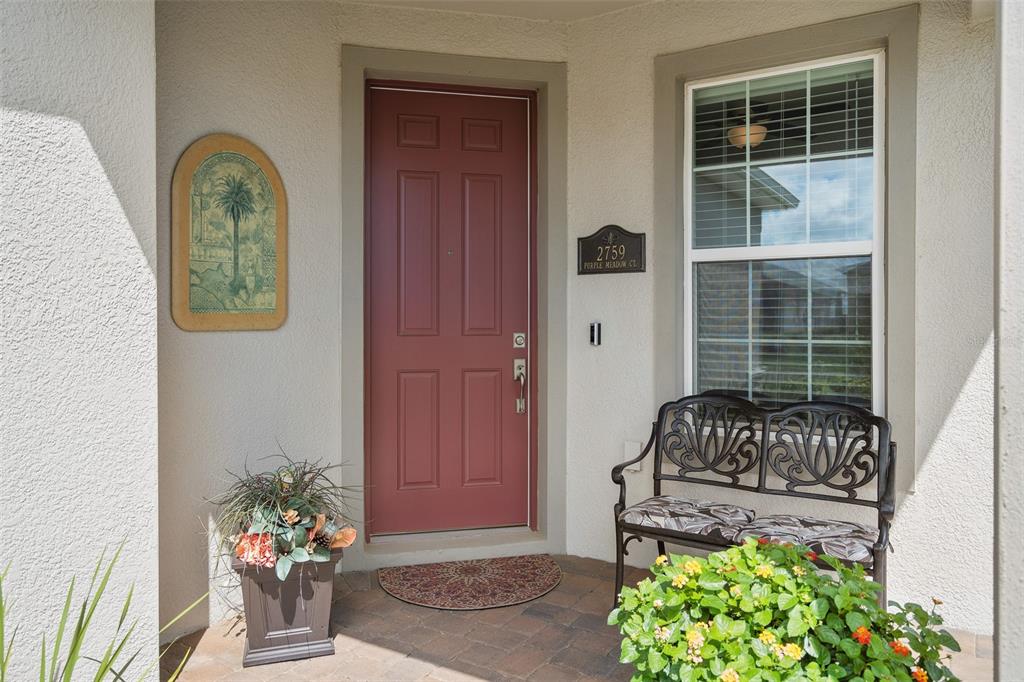 A front porch features a red door, a metal bench, a potted plant, and wall decor — 2759 PURPLE MEADOW COURT, MINNEOLA, FL
