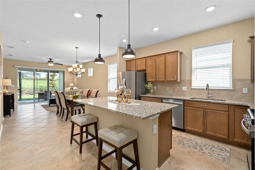 A kitchen with granite countertops and an island opens into a dining area and patio — 2759 PURPLE MEADOW COURT, MINNEOLA, FL