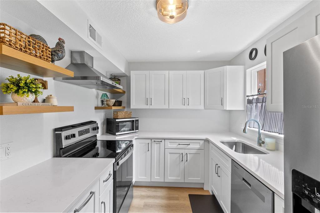 A kitchen features white cabinets, quartz countertops, stainless steel appliances, and floating wood shelves — 267 CROWN OAKS WAY UNIT 267, LONGWOOD, FL