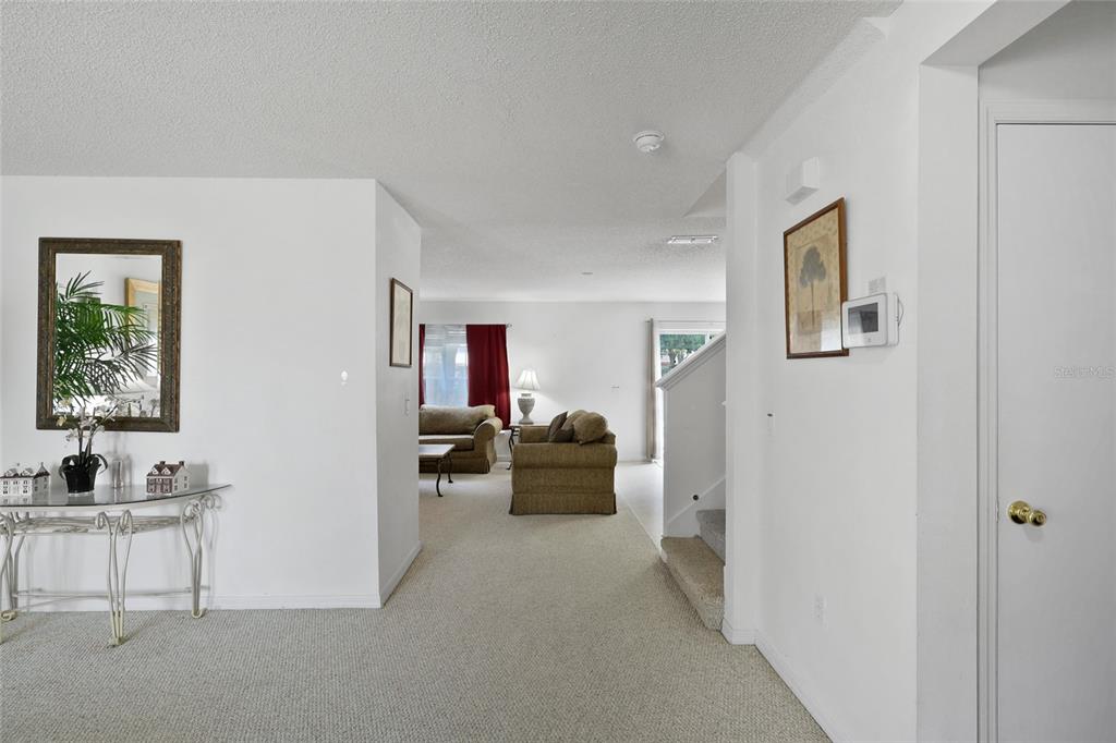 A carpeted living area features a white hallway, a staircase, and a console table — 16816 RISING STAR DRIVE, CLERMONT, FL
