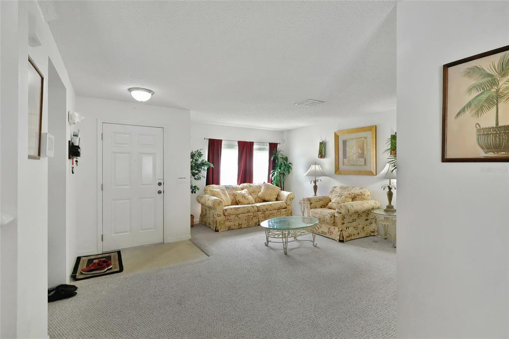 A living room with beige carpet, floral furniture, and a white front door — 16816 RISING STAR DRIVE, CLERMONT, FL