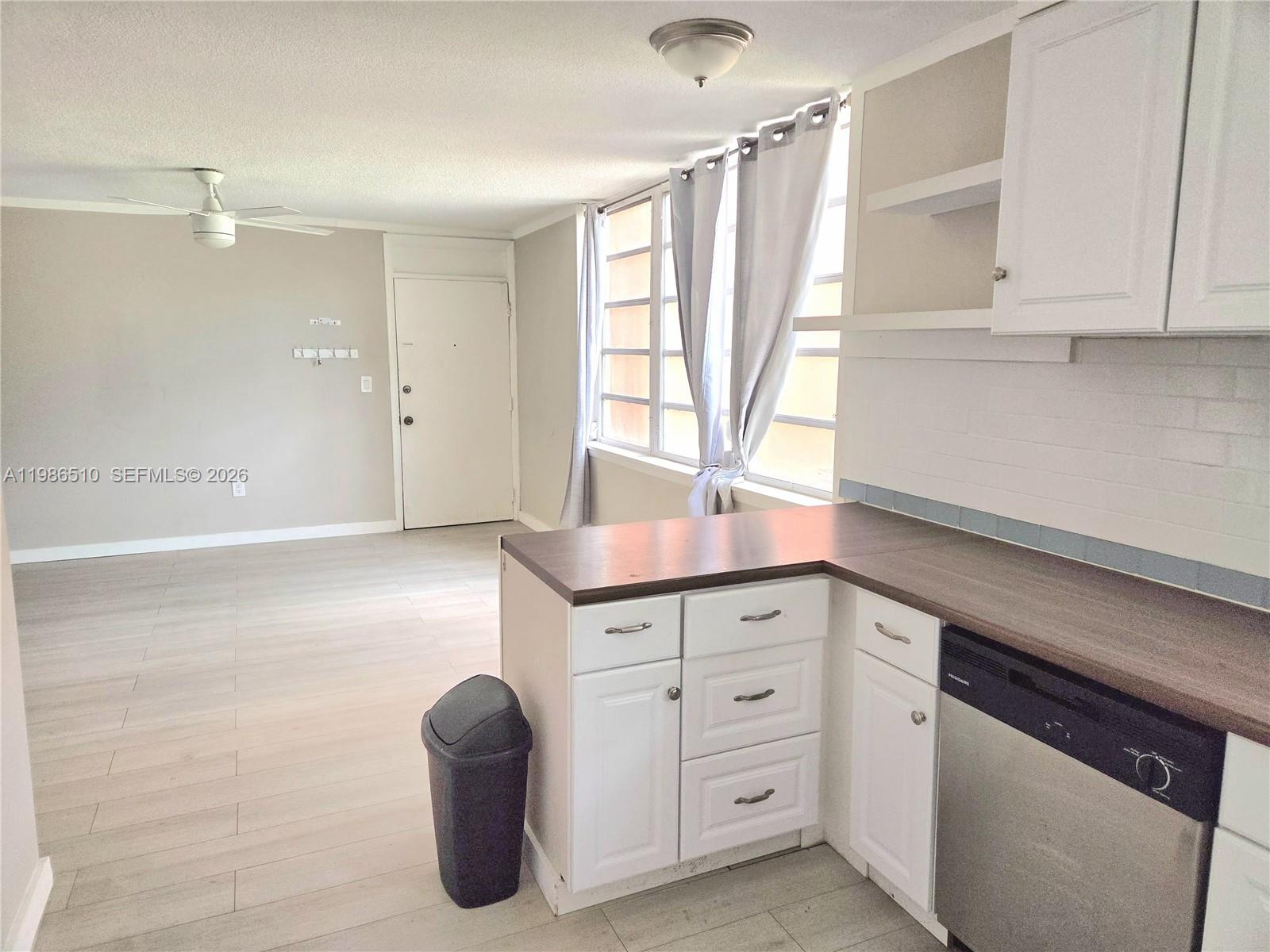 A kitchen with white cabinets and a dishwasher overlooks an open living area — 1700 NE 191st St # 100, Miami FL 33179, MIAMI, FL