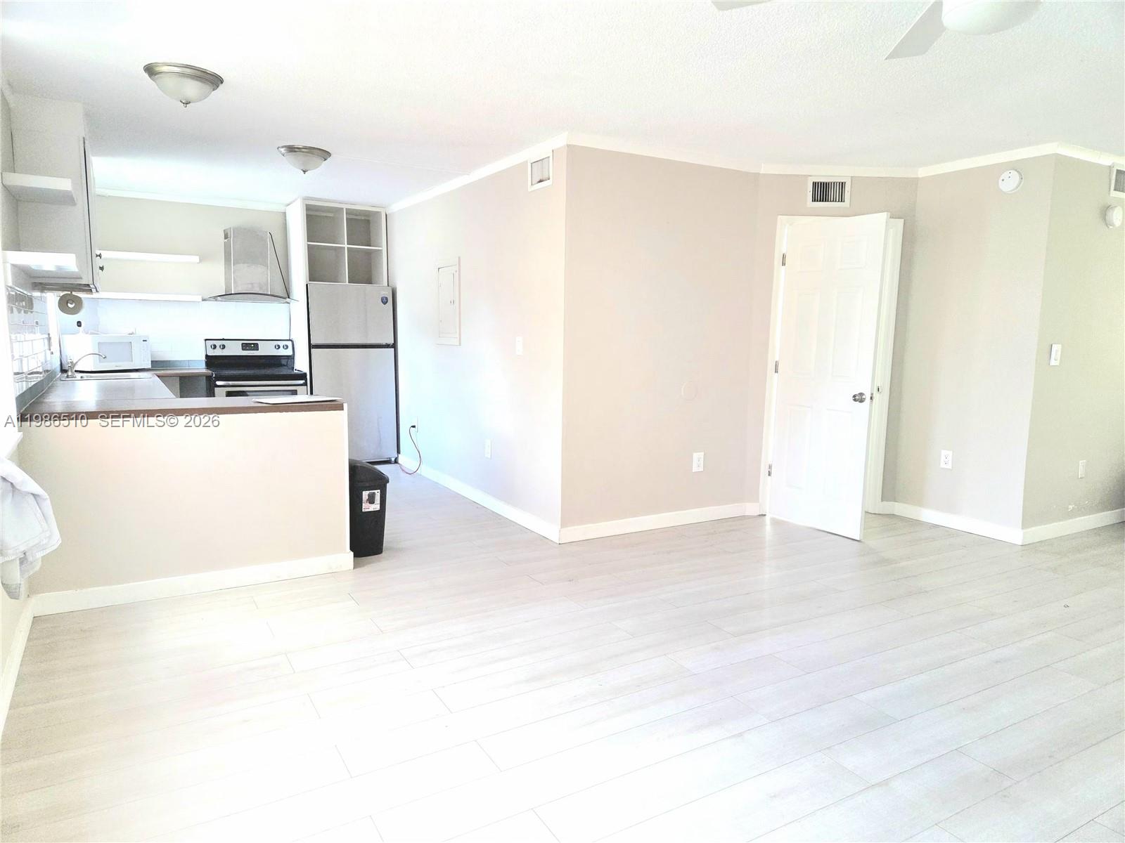 An open-concept kitchen with stainless steel appliances connects to a living area with light flooring — 1700 NE 191st St # 100, Miami FL 33179, MIAMI, FL