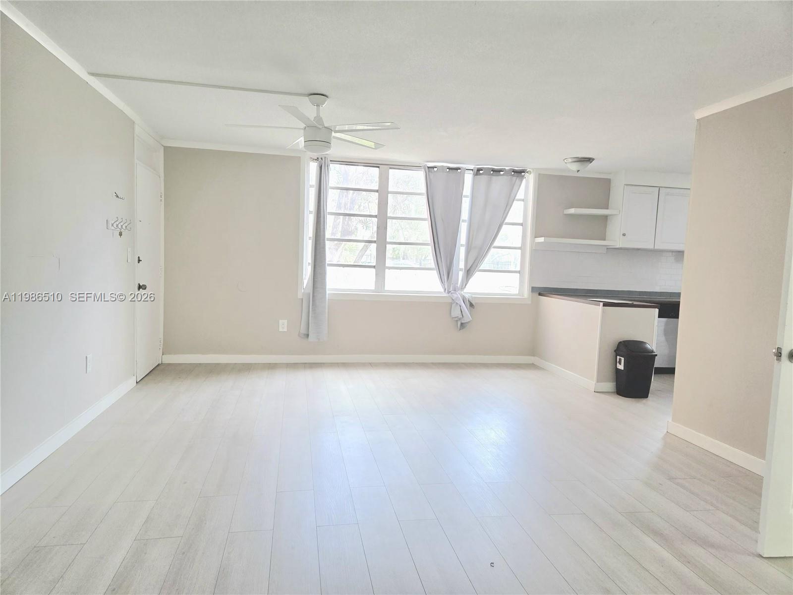 An open-concept living area features light wood-look flooring, a ceiling fan, and an adjacent kitchen — 1700 NE 191st St # 100, Miami FL 33179, MIAMI, FL