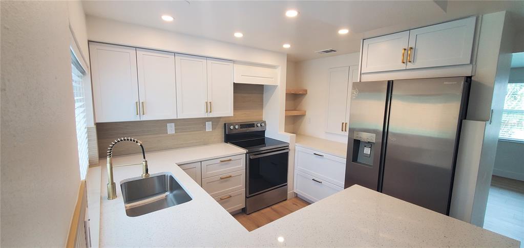A modern kitchen features white cabinets, stainless steel appliances, and light-colored quartz countertops — 3611 SHERYL HILL DRIVE, HOLIDAY, FL