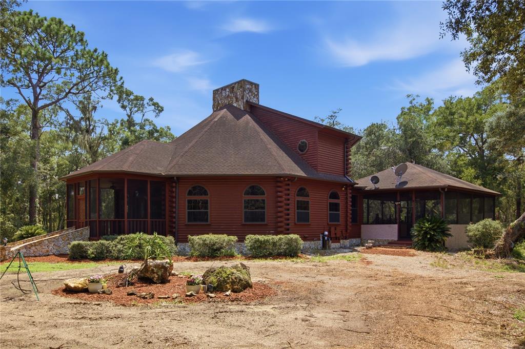 A two-story log cabin with a stone chimney and screened porches sits on a dirt lot — 6850 ROUND LAKE ROAD, MOUNT DORA, FL