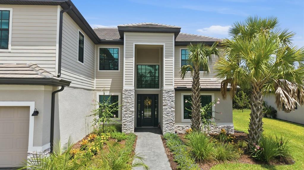 A two-story house exterior features beige siding, stone accents, a front walkway, and palm trees — 11035 HANGING VINE DRIVE, FORT MYERS, FL