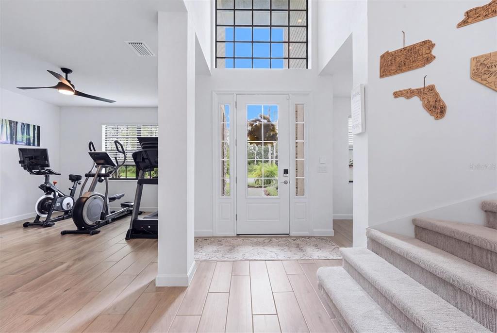 A bright entryway features a tall window, white front door, wood-look flooring, and carpeted stairs — 11035 HANGING VINE DRIVE, FORT MYERS, FL