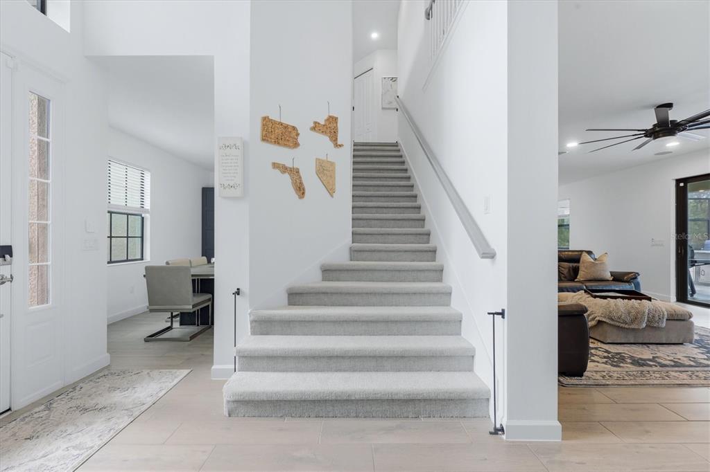 A bright entryway features a carpeted staircase, white walls, and wood-look tile flooring — 11035 HANGING VINE DRIVE, FORT MYERS, FL