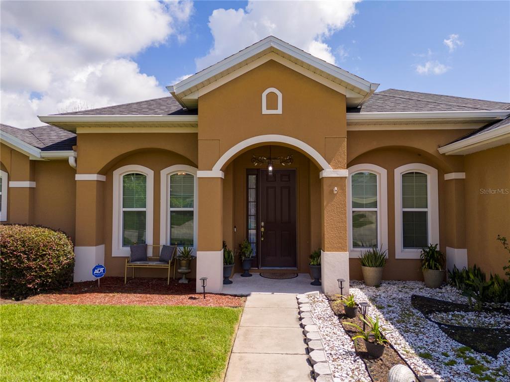 The exterior of a tan stucco house features a covered entryway and a concrete walkway — 603 BRITTLE FERN AVENUE, DELAND, FL