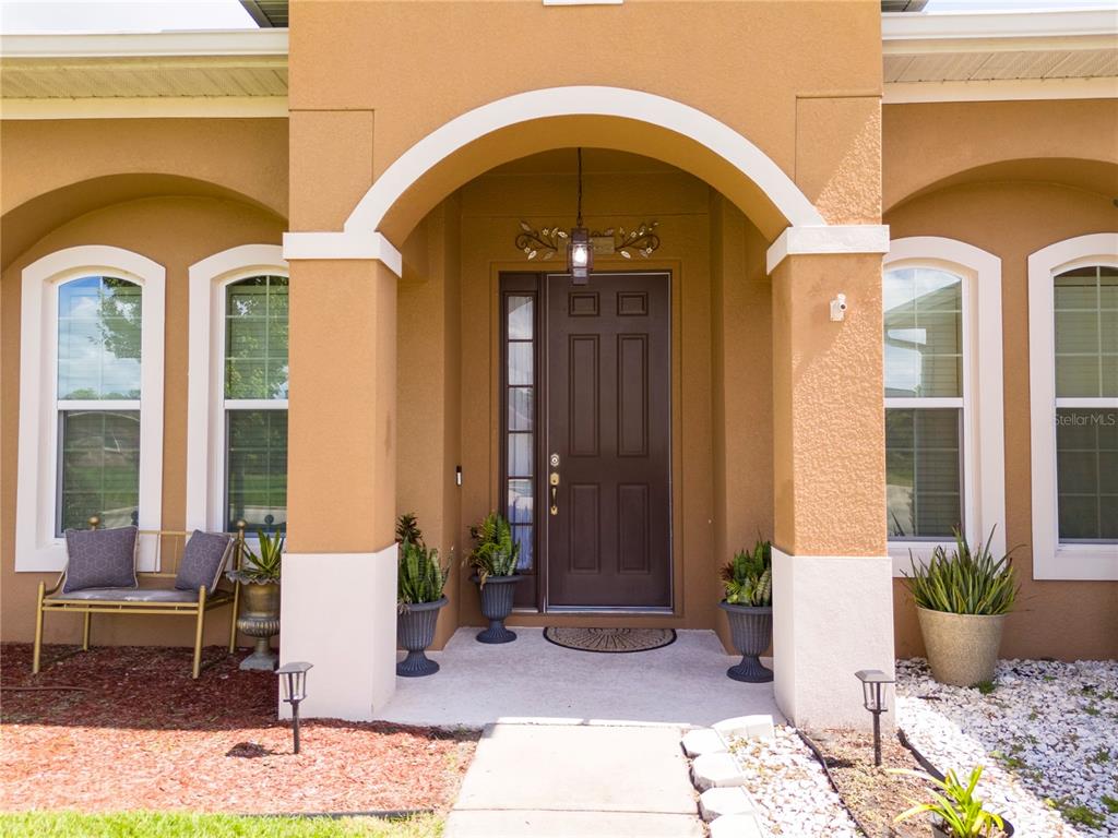 The front entrance of a house features a brown door, arched entryway, and potted plants — 603 BRITTLE FERN AVENUE, DELAND, FL