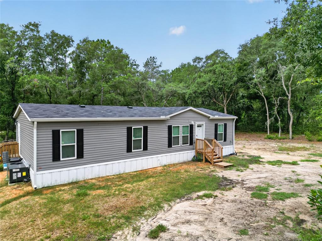A grey manufactured home with black shutters sits on a sandy lot near trees — 259 OAK STREET, HAWTHORNE, FL