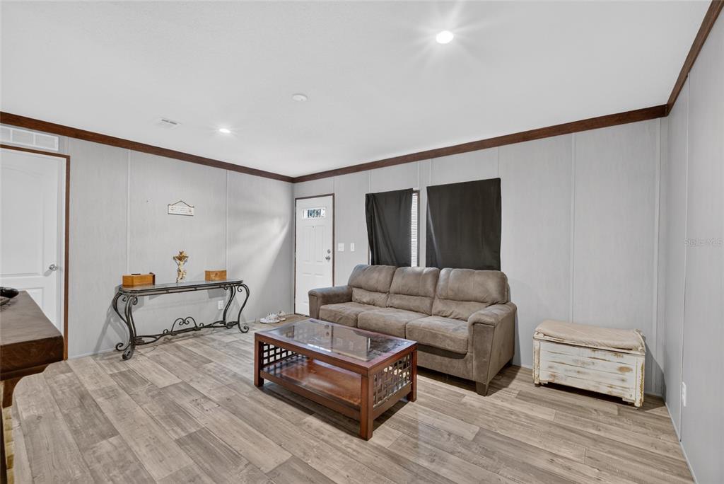 A living room features gray paneled walls, wood-look flooring, a brown sofa, and a coffee table — 259 OAK STREET, HAWTHORNE, FL