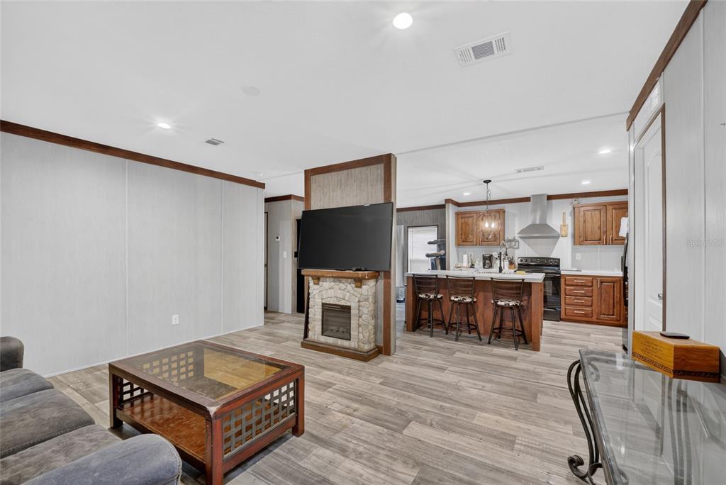 An open-concept living room and kitchen featuring wood-look flooring, a stone fireplace, and bar seating — 259 OAK STREET, HAWTHORNE, FL