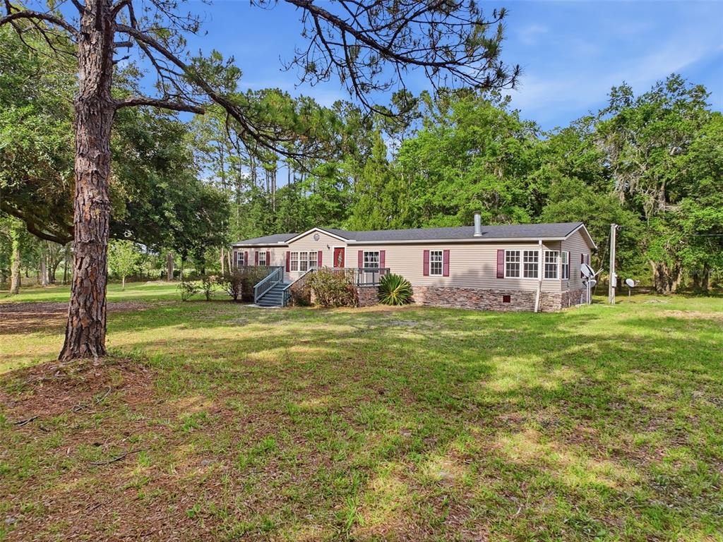A single-story manufactured home with tan siding and a stone base sits on a lawn — 17926 SE 49TH PLACE, HAWTHORNE, FL