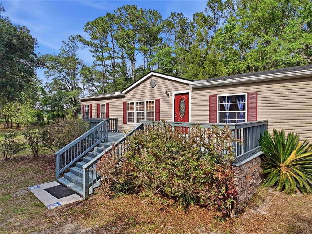 A tan manufactured home features a red front door, a wooden deck, and stone skirting — 17926 SE 49TH PLACE, HAWTHORNE, FL
