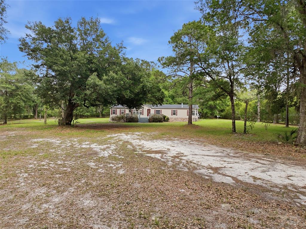 A single-story house sits on a large, grassy lot surrounded by many mature trees — 17926 SE 49TH PLACE, HAWTHORNE, FL