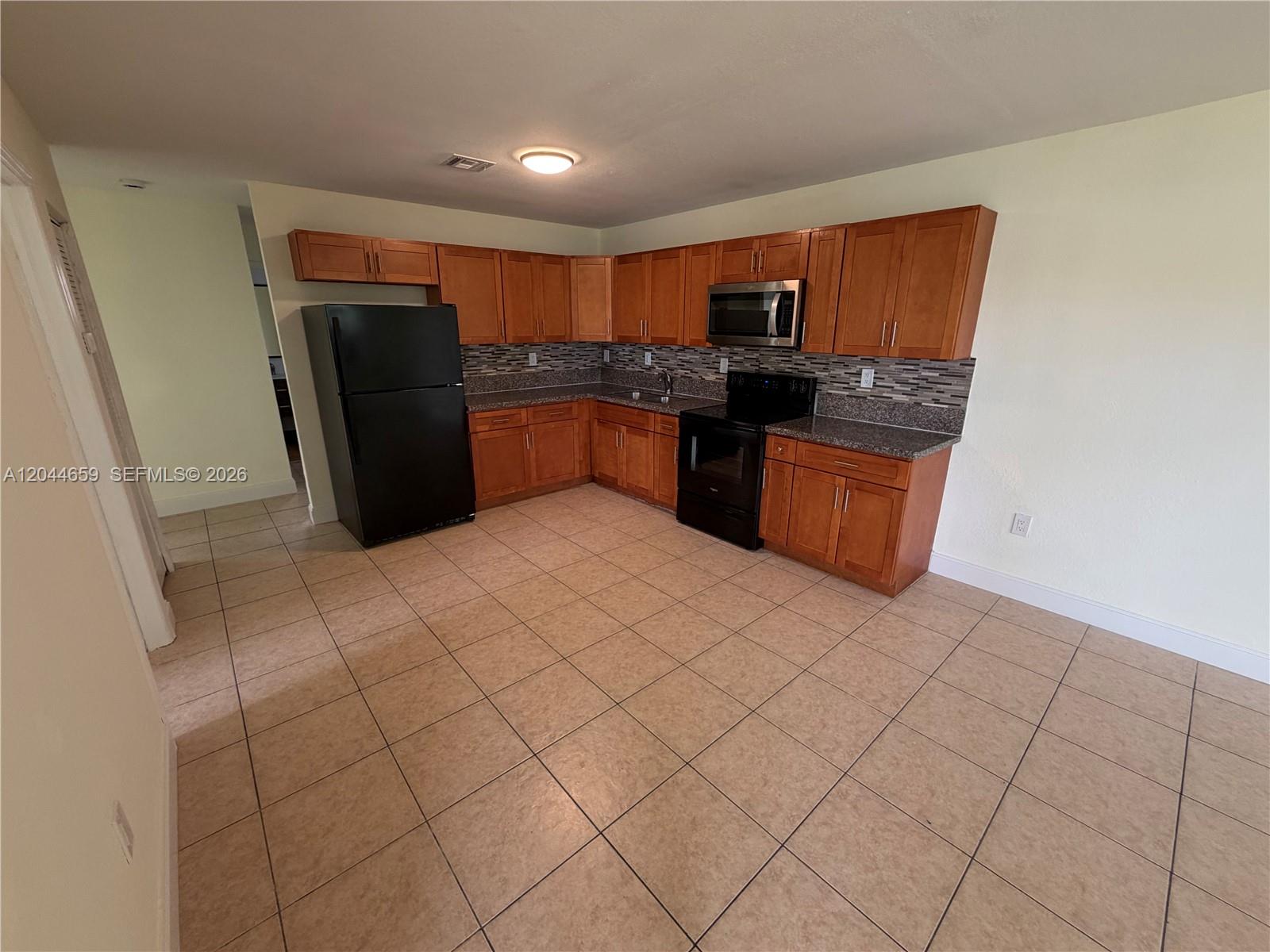 A kitchen features wooden cabinets, black appliances, granite countertops, and light-colored tile flooring — 10530 SW 183rd St # 2, Miami FL 33157, MIAMI, FL