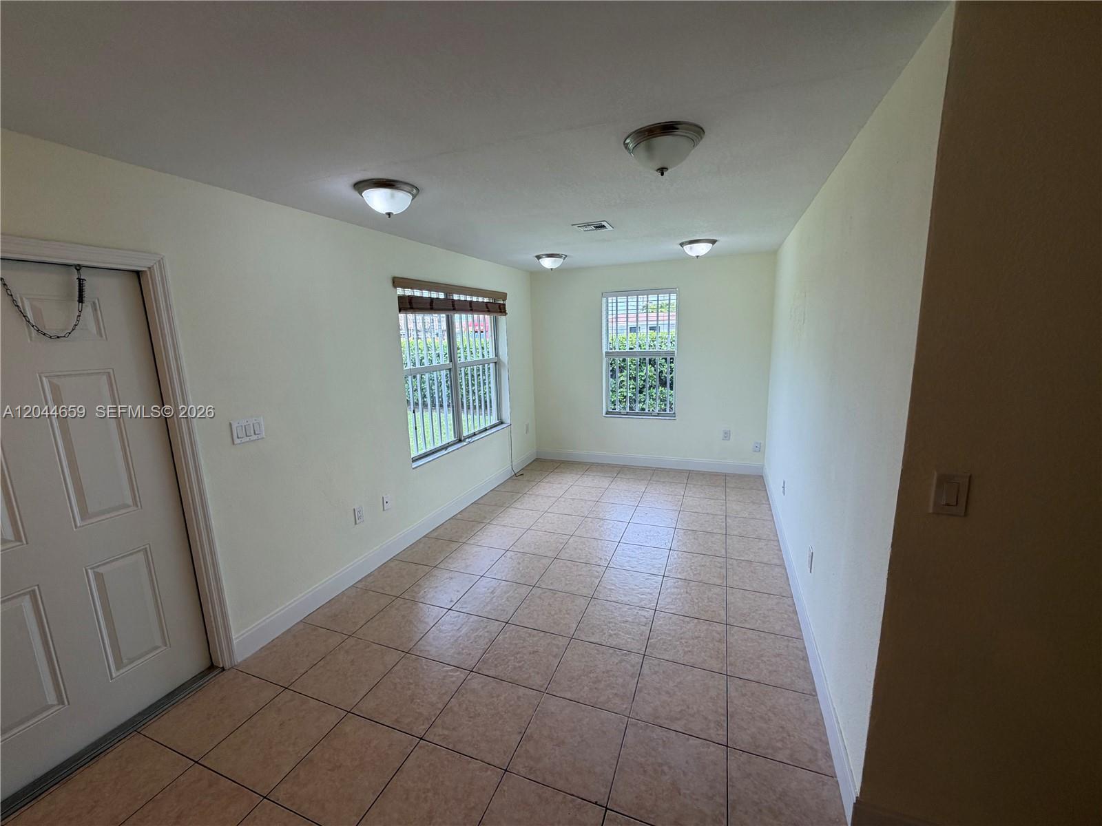 An empty room features light-colored walls, tiled flooring, three ceiling lights, and two windows — 10530 SW 183rd St # 2, Miami FL 33157, MIAMI, FL