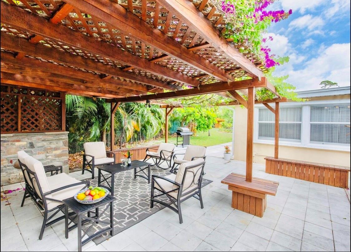 A patio features a wooden pergola, outdoor furniture, and a stone wall on a tiled floor — 279 Hach Lane, West Palm Beach FL 33415, WEST PALM BEACH, FL
